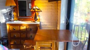 A room with a wooden desk and chair, a dresser, a mirror, and a television mounted on the wall.