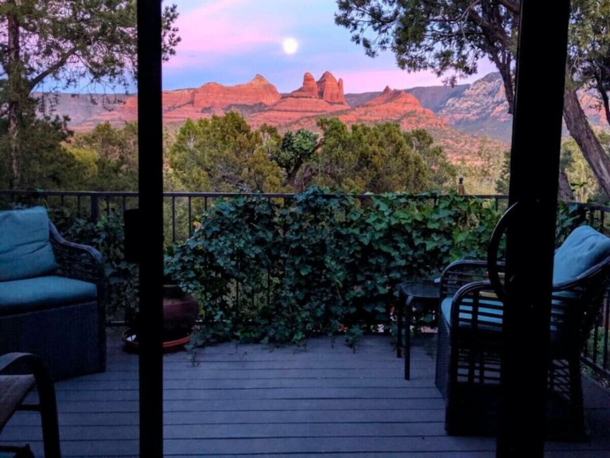 A deck with outdoor furniture, a view of red rock formations, and a moon in the sky.