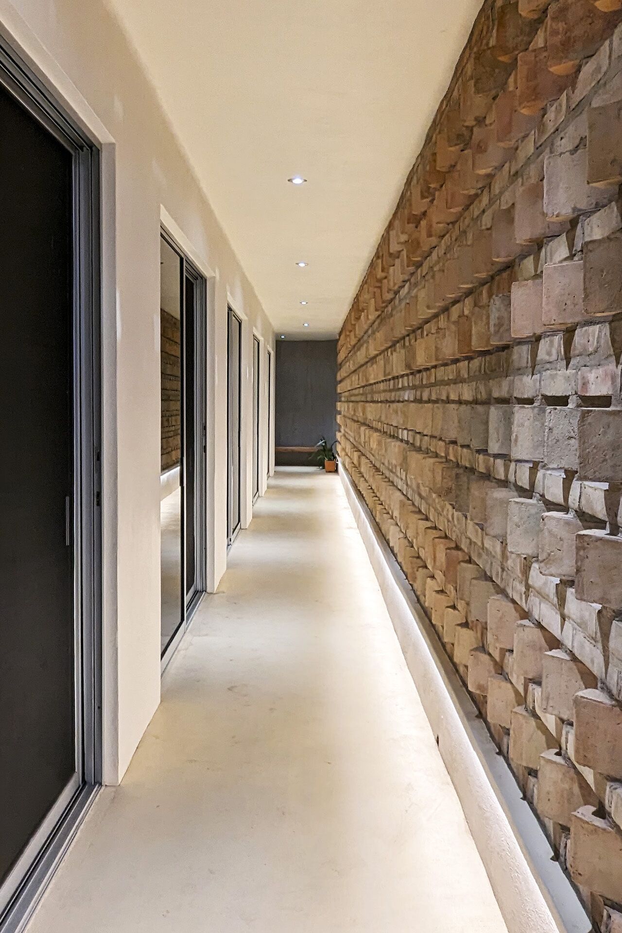 A hallway with a brick wall on one side and glass doors on the other.