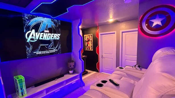 A room with a large flat-screen TV displaying 'Avengers: Endgame', a white couch, a small figurine, and a Captain America shield on the wall.