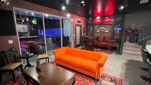A cozy lounge area with a bright orange sofa, a wooden coffee table, and a patterned rug. There are glass doors leading to an outdoor seating area.