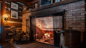 A fireplace with logs, a dog, and a metal pot on the right. - Uncle Tom's 3BDR Cabin For Nature Lover (Grayling)
