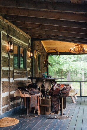 L’intérieur d’un chalet rustique, avec des murs en bois, une véranda en bois et une table sur laquelle sont posés des selles en cuir.