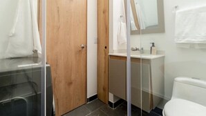 Une salle de bain avec une porte en bois, une cabine de douche en verre, un lavabo blanc et des toilettes.