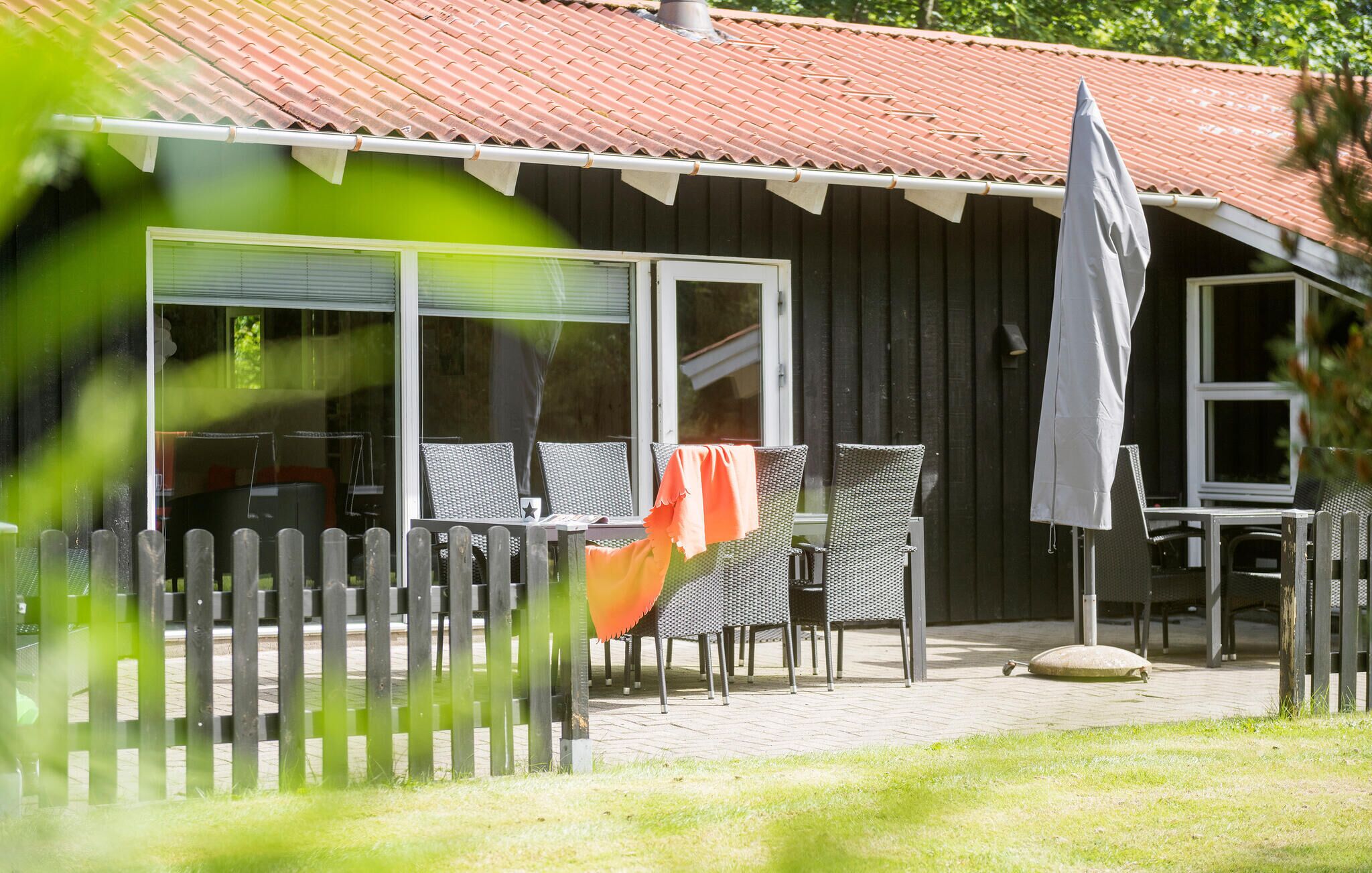 Un bâtiment en bois avec un toit recouvert de tuiles, des tables et des chaises disposées à l’extérieur pour créer un espace de détente, et une clôture en bois.