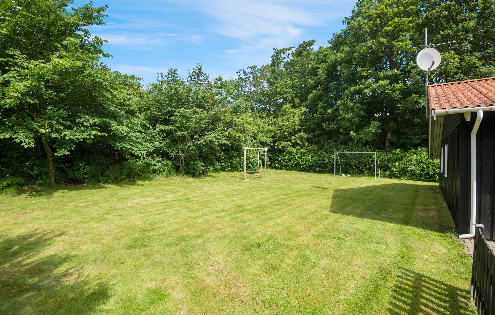 A well-maintained grassy backyard with two soccer goals, surrounded by dense trees and a house with a tiled roof.