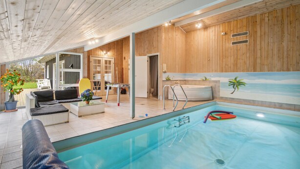 Een binnenzwembad met houten plafond en wanden, een jacuzzi en uitzicht op de omgeving.