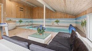 Een kamer met een zwembad, houten wanden, een bank en een tafel met bloemen.