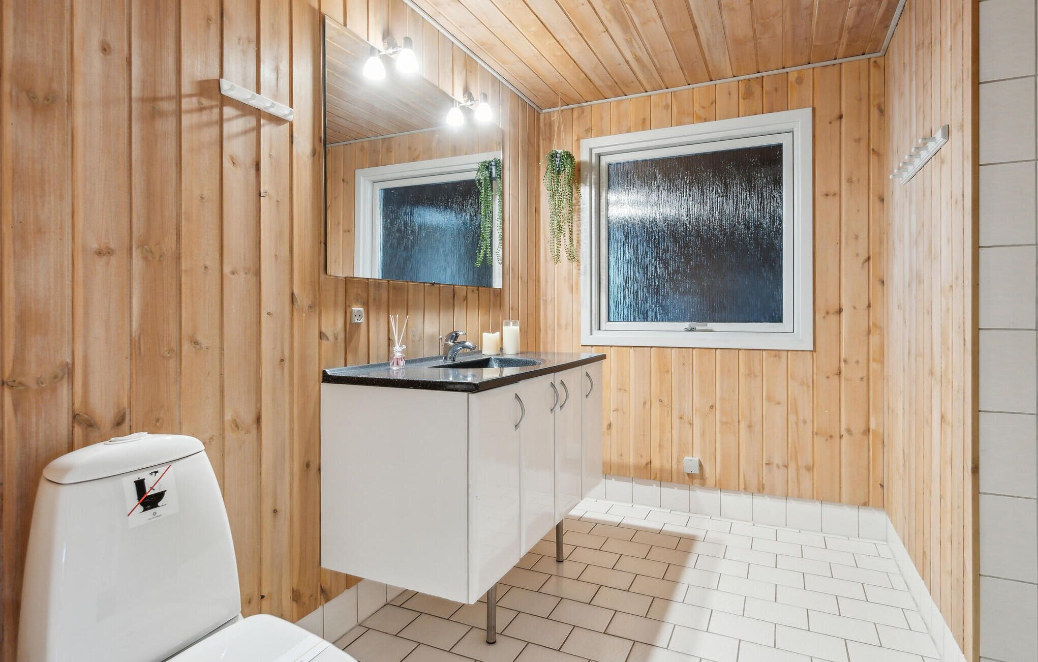 A bathroom with wooden walls, a white sink, a mirror, and a window with a view of rain.