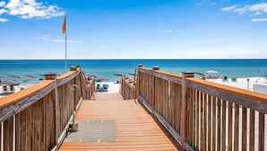 A wooden deck leading to a beach with umbrellas and lounge chairs. - Palacio 1402 | Beachfront | My Beach Getaways (Pensacola)