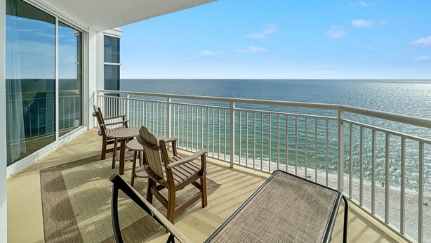 A balcony with a view of the ocean, furnished with a table and chairs, and a glass door leading to a room. - Palacio 1402 | Beachfront | My Beach Getaways (Pensacola)
