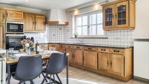 A kitchen with wooden cabinets, a built-in oven, a window, and a dining area with chairs and a table set for two.