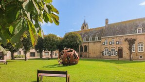 A grassy courtyard with a bench, a large spherical sculpture, and a historic building with multiple windows and a tower.