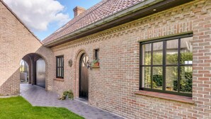 A brick house with a covered patio, a large window, and a door with a wreath.