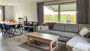 A modern living room with a grey sofa, a wooden coffee table, and a dining area with a wooden table and chairs.