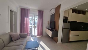 A modern living room with a sofa, a coffee table, a TV, and a kitchen area with a refrigerator and microwave.