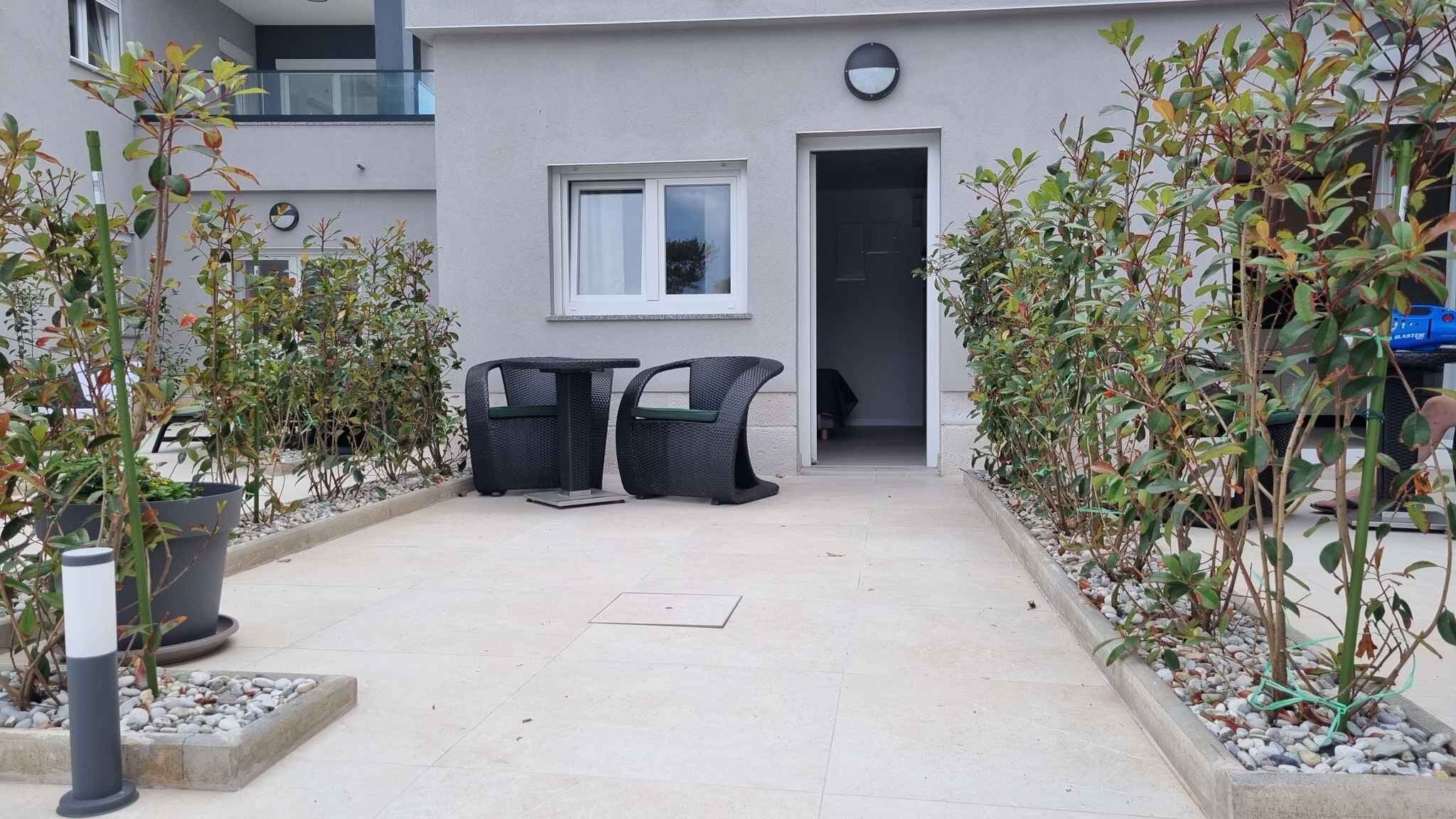 A courtyard with two wicker chairs, a small table, and potted plants.