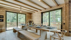 A wooden interior with a long dining table set for four, benches, and a chair. Large windows offer views of the outdoors. - Chalet, fitness, swimming pool, sauna, fireplace or stove, parking, tv, 250m², Morzine (Morzine)