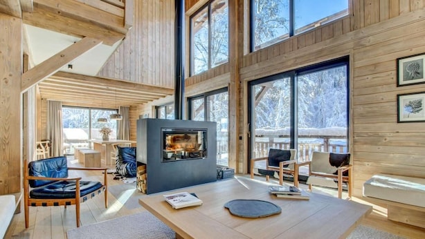 A spacious living area with a fireplace, wooden furniture, and large windows offering a view of the snowy outdoors. - Chalet, fitness, swimming pool, sauna, fireplace or stove, parking, tv, 250m², Morzine (Morzine)