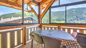 A wooden deck with a table and chairs, large windows offering a view of a forested mountain. - 2nd floor, balcony, tv, 60m², Morzine (Morzine)