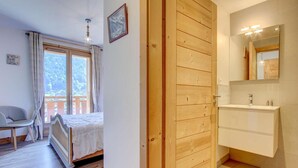 A bedroom with a bed, a chair, a wooden door, and a bathroom with a sink and mirror. - 2nd floor, balcony, tv, 60m², Morzine (Morzine)