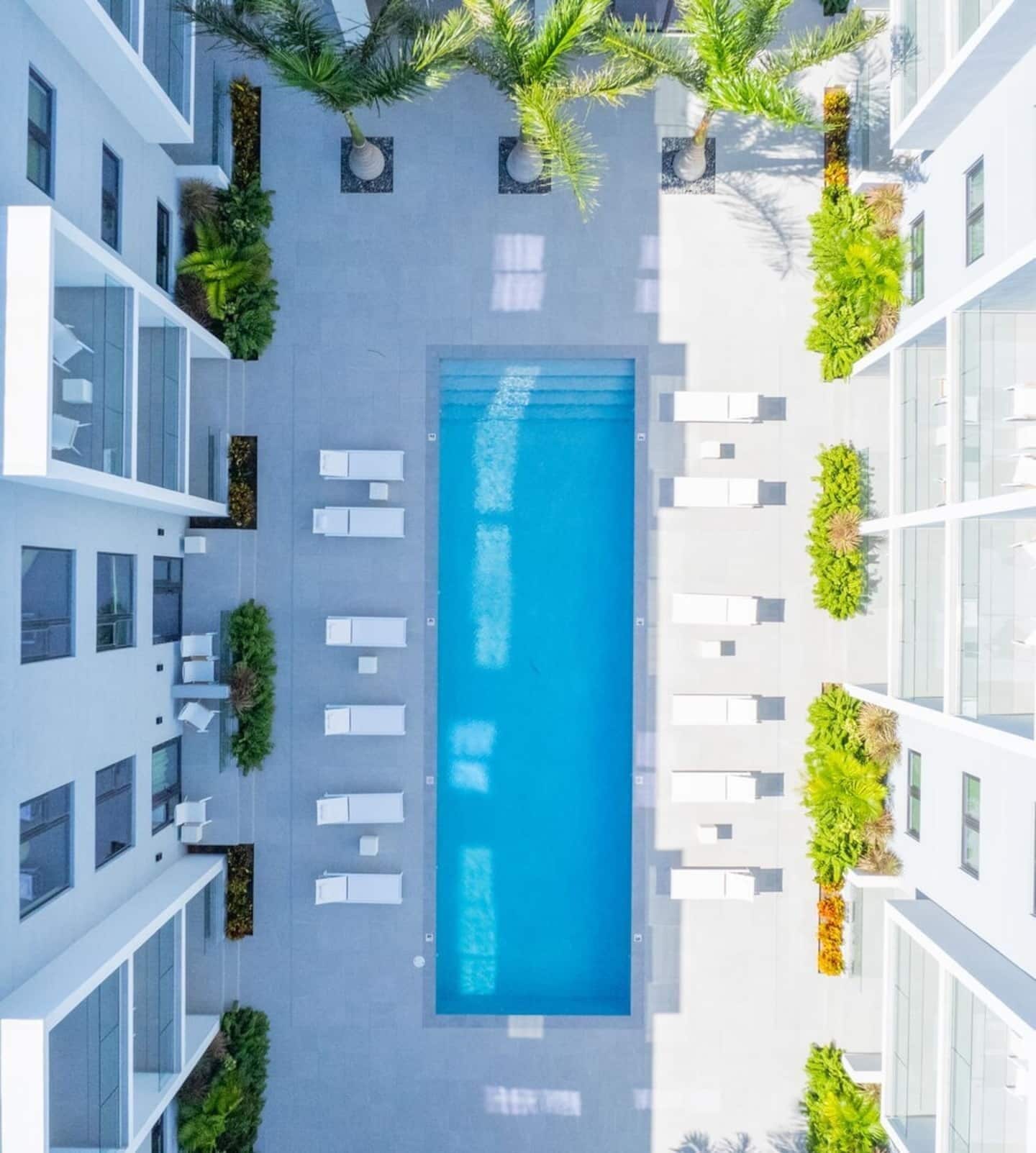 Vue aérienne d’un hôtel moderne doté d’une piscine centrale, entourée d’espaces de détente et de verdure.