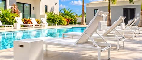 Ett område vid poolen med solstolar, en pool och en modern byggnad med stora fönster.