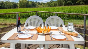 Une table dressée à l’extérieur, avec des assiettes, des couverts, une bouteille, un pichet et une miche de pain.