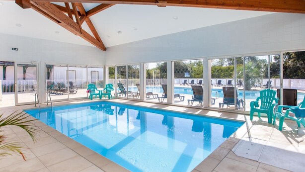 Une piscine intérieure aux parois en verre transparent, entourée de chaises longues et dotée d’un sol carrelé.