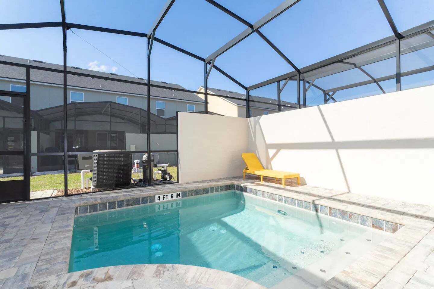 Une piscine intérieure protégée par une paroi de verre, un fauteuil de relaxation jaune et une vue dégagée sur les bâtiments environnants.