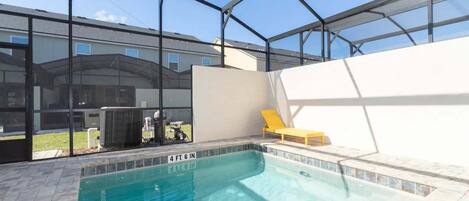Une piscine intérieure protégée par une paroi de verre, un fauteuil de relaxation jaune et une vue dégagée sur les bâtiments environnants.