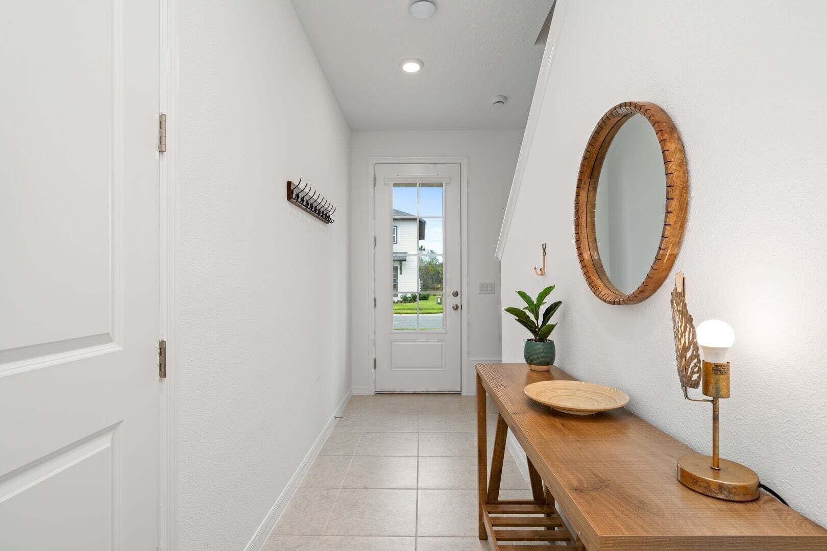 A hallway with a wooden bench, a round mirror, a potted plant, and a door leading to a room.