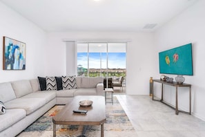 A modern living room with a sectional sofa, a coffee table, a TV, and a balcony with a view.