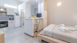 Une chambre d’hôtel moderne équipée d’une kitchenette, d’un lit avec des serviettes, d’un bureau avec un ordinateur et d’une salle de bain avec douche.