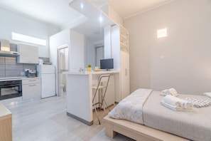 Een moderne hotelkamer met een kitchenette, een bed met handdoeken, een bureau met een computer en een badkamer met douche.