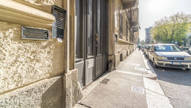 Une vue de rue avec un immeuble qui se distingue par une grande porte noire et une plaque fixée au mur.