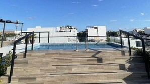 Ein Pool auf dem Dach mit Stufen, umgeben von modernen Gebäuden und blauem Himmel.
