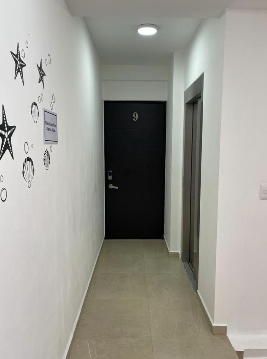 Un couloir avec une porte noire portant le numéro « 9 », un panneau sur le mur et un mur décoré de motifs représentant des étoiles et des coquillages.