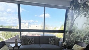 Ein Wohnzimmer mit einer Couch, zwei Sesseln, einem Couchtisch und einem großen Fenster mit Blick auf die Stadt.