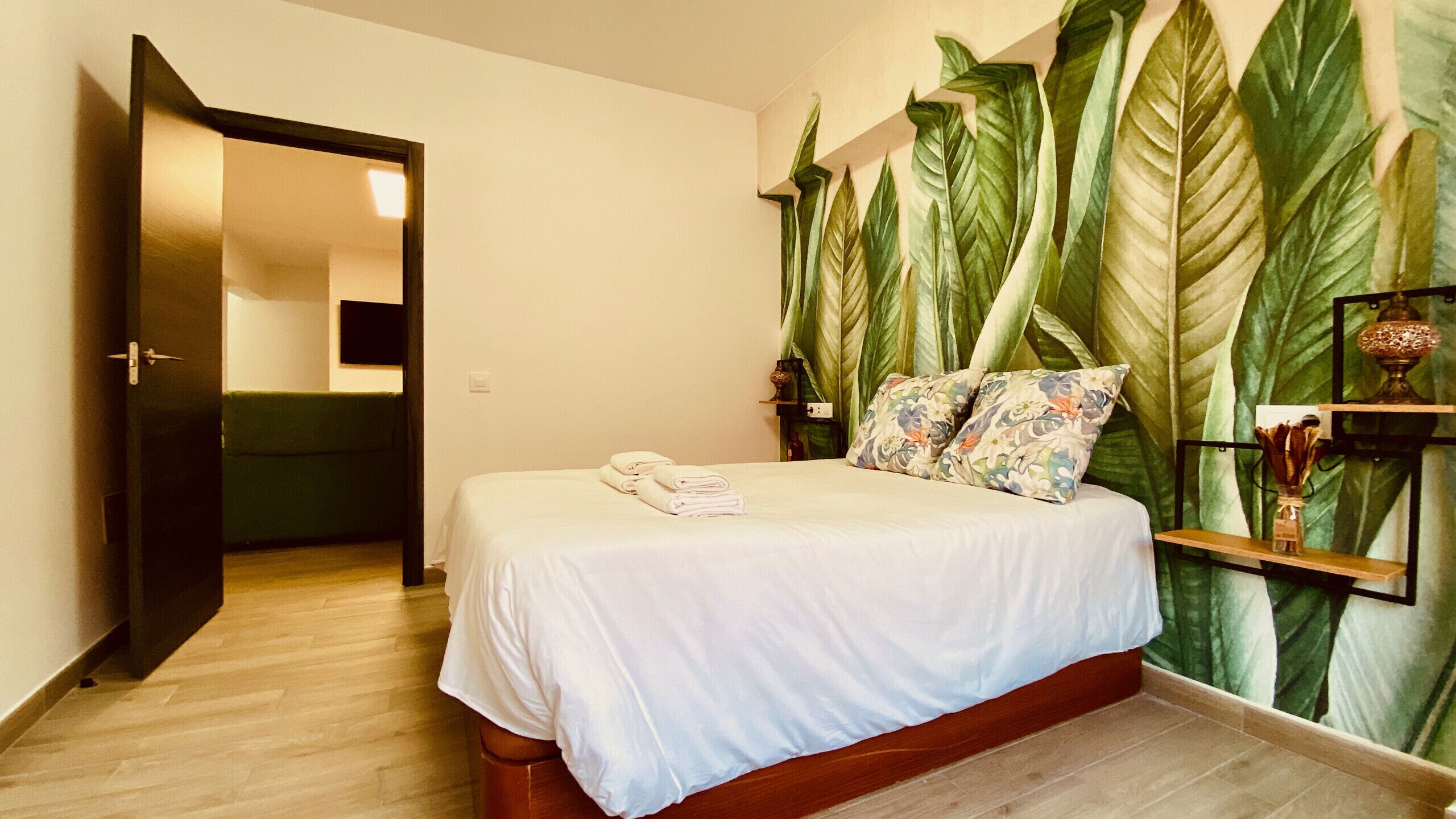 A hotel room with a bed, a green couch, a wall-mounted TV, and a large window with curtains.