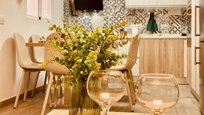 A dining area with a table set for two, featuring a vase with green foliage and two wine glasses.