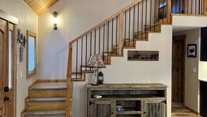 Uma escada de madeira leva a um mezanino, com uma mesa consola e uma luminária na parede.