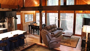 Interior de cabana com cozinha, sala de jantar, sofá e lareira.