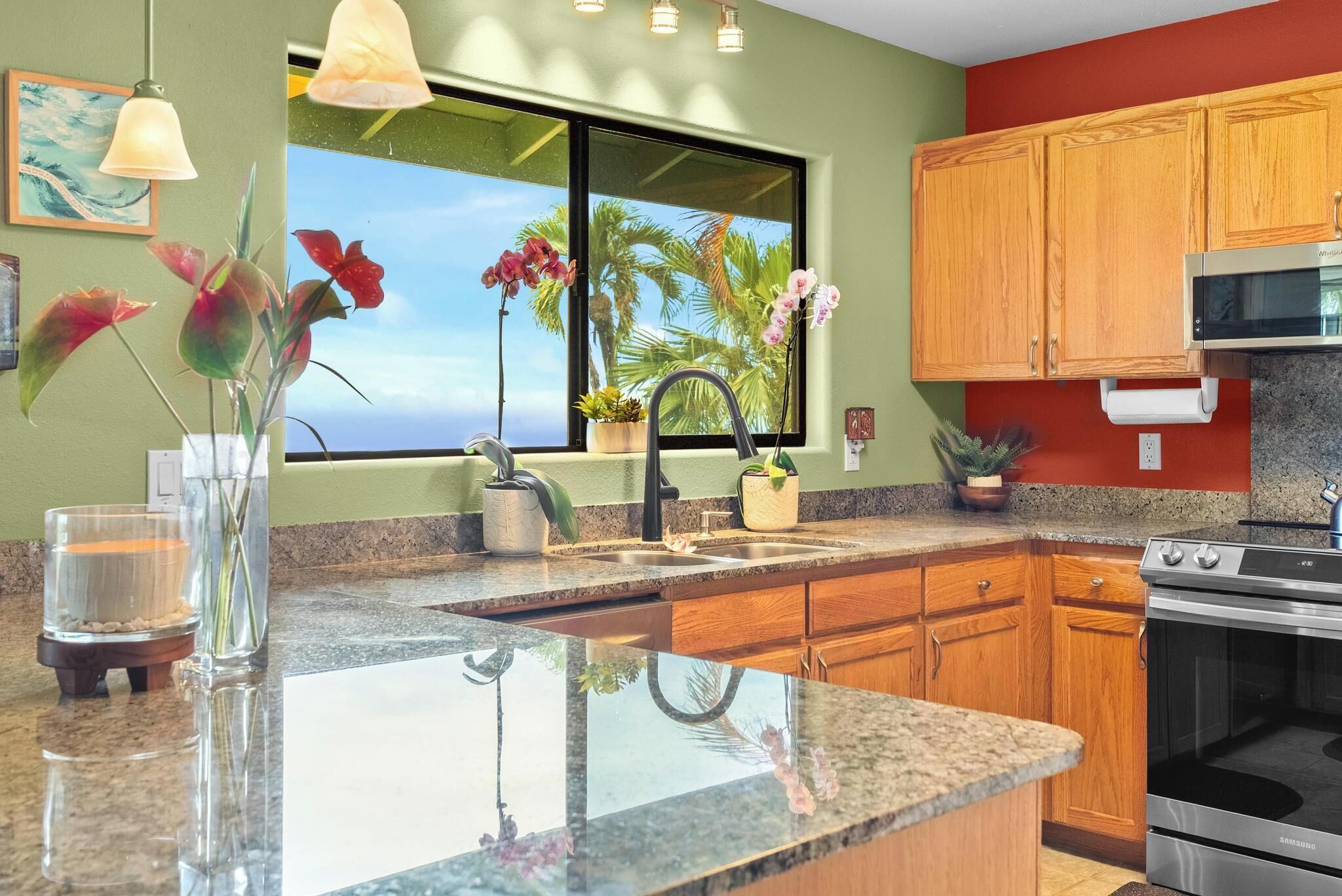 A kitchen with a granite countertop, wooden cabinets, a stainless steel stove, and a window with a view of palm trees.