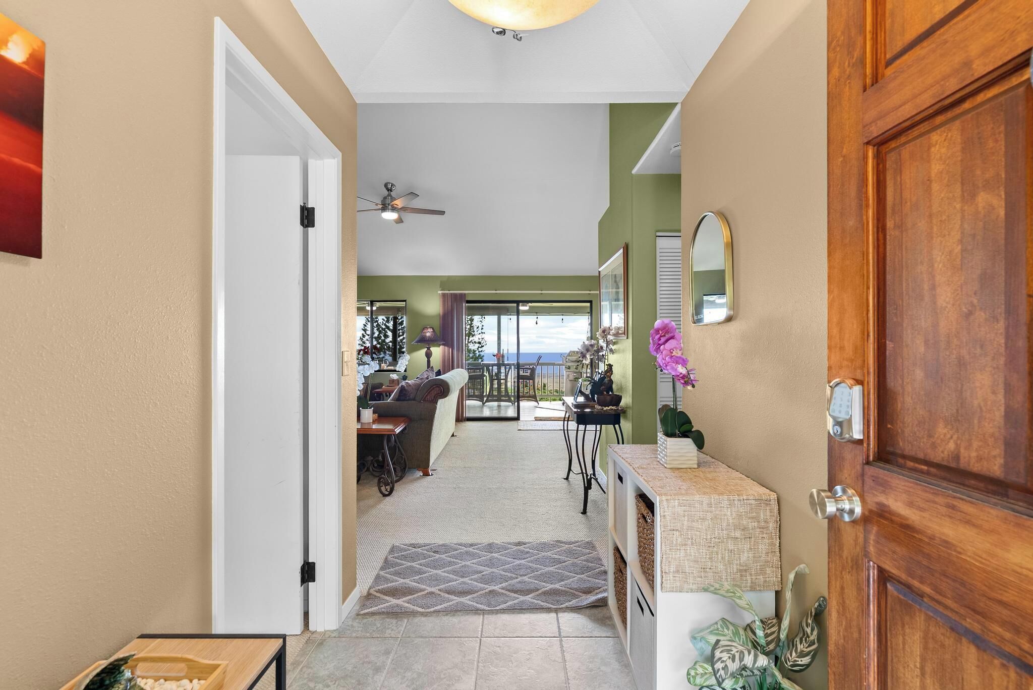 A hallway leading to a dining area with a view of the ocean, a ceiling fan, and a wooden door.