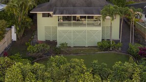 A single-story building with a balcony, surrounded by lush greenery and a small pond.
