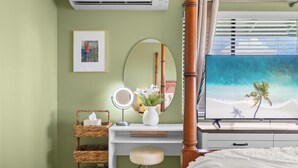 A bedroom with a bed, a vanity with a mirror, a dresser, a wall-mounted air conditioner, and a window with a beach view.