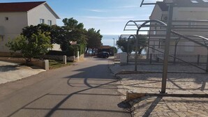 A residential street with houses, a parked car, and a clear view of the sea. - Holiday apartment mit Terrasse (Ivan Dolac)