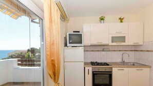 A compact kitchen with a gas stove, oven, and a small TV on a white cabinet. - Holiday apartment mit Terrasse (Ivan Dolac)