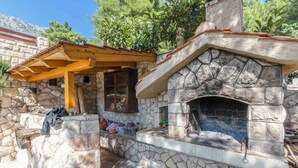 A stone-built outdoor kitchen with a chimney, a wooden pergola, and a stone bench. - Holiday apartment mit Terrasse (Ivan Dolac)